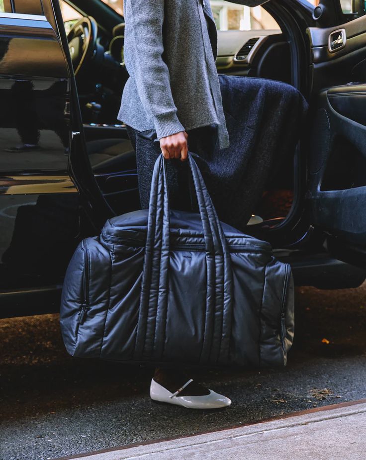 a man carrying a large black duffel bag in front of a car with the door open