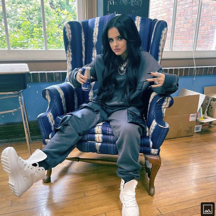 a woman sitting in a blue chair with white sneakers on her feet and holding a cell phone