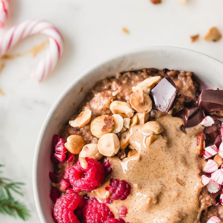 a bowl filled with oatmeal, raspberries and candy canes