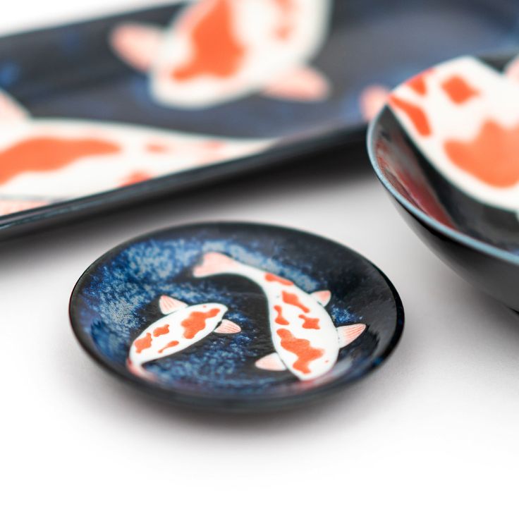 two plates with fish painted on them sitting next to each other in front of one another