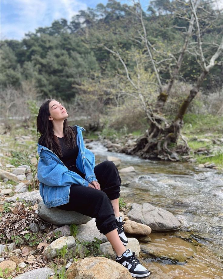 a woman sitting on top of a rock next to a river