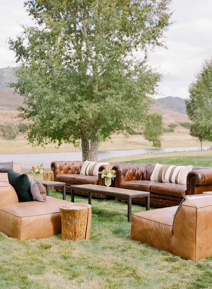 an outdoor seating area with leather couches and tables in the grass near a tree