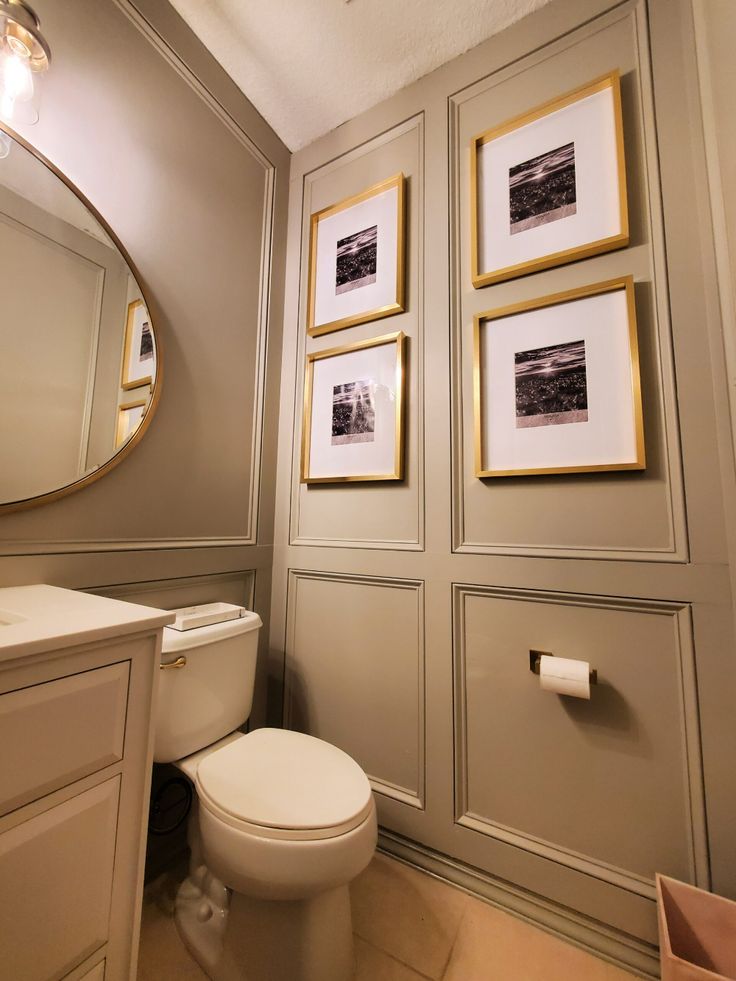 a white toilet sitting in a bathroom next to a sink and a wall with pictures on it