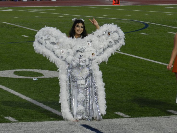 a woman dressed in white and silver stands on a football field