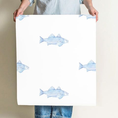 a person holding up a white paper with blue fish on it