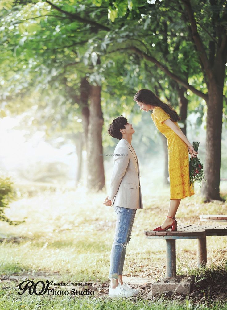 a woman in yellow dress standing next to a man on a bench