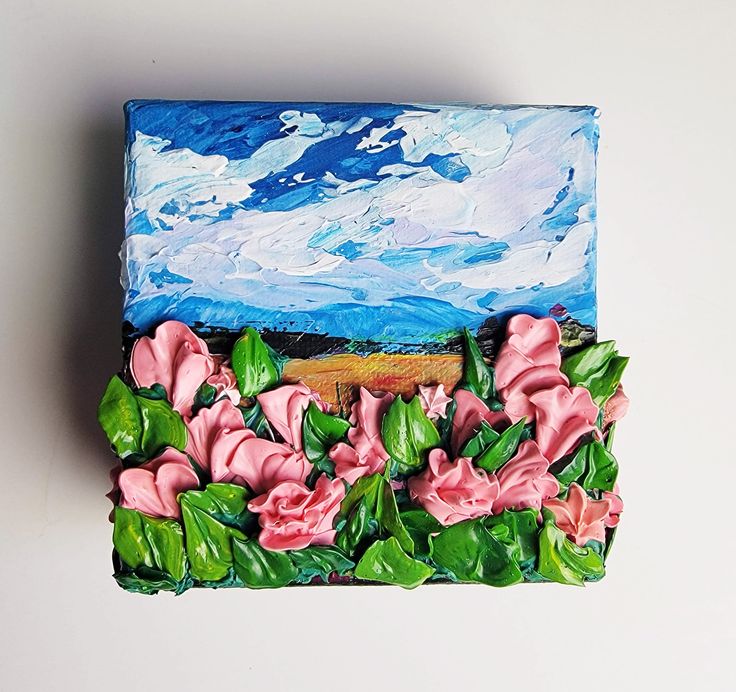 a painting of pink flowers and green leaves on top of a blue box with clouds in the background