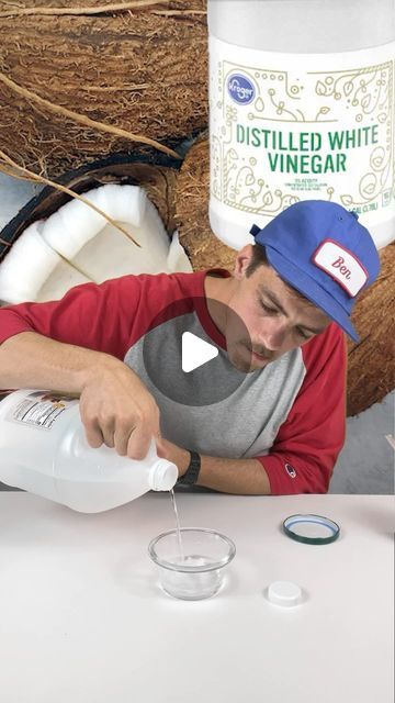 a man pouring something into a glass on top of a white table next to coconuts