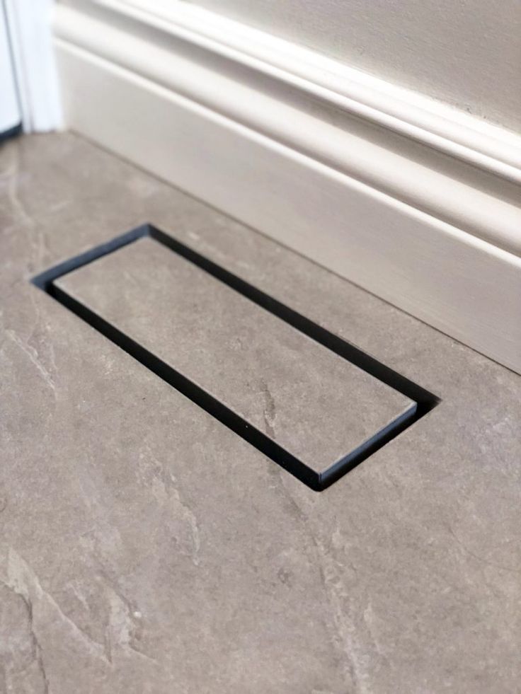 a square metal object sitting on the floor in front of a white door with black trim