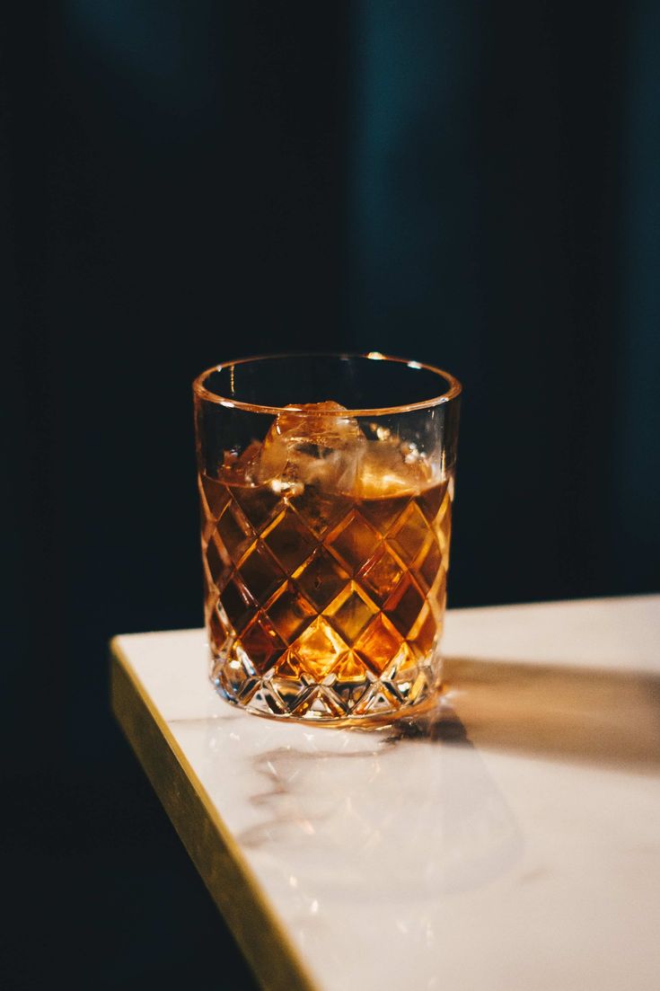 an old fashioned whiskey glass sitting on top of a white counter next to a bottle