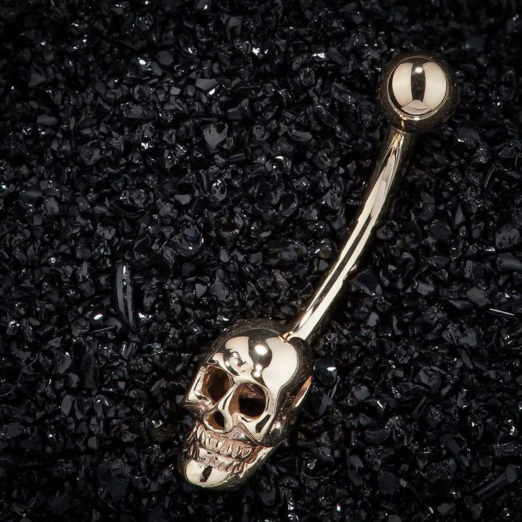 a gold colored skull belly button ring with a ball in the middle on black gravel