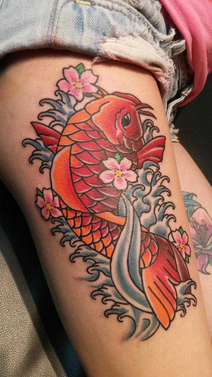 a woman's thigh with a koi fish tattoo on it and flowers in the background