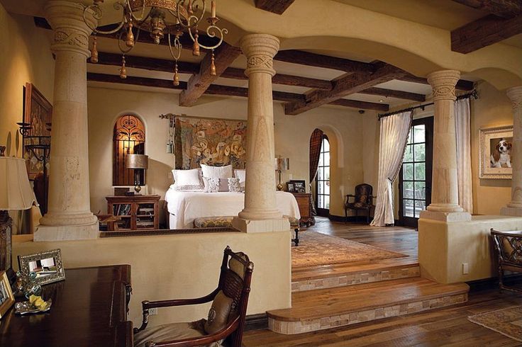 an elegant bedroom with columns and chandelier in the center, along with wooden flooring