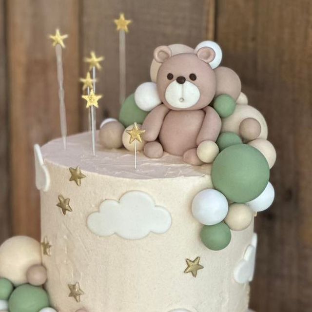 a teddy bear sitting on top of a white cake with stars and clouds around it