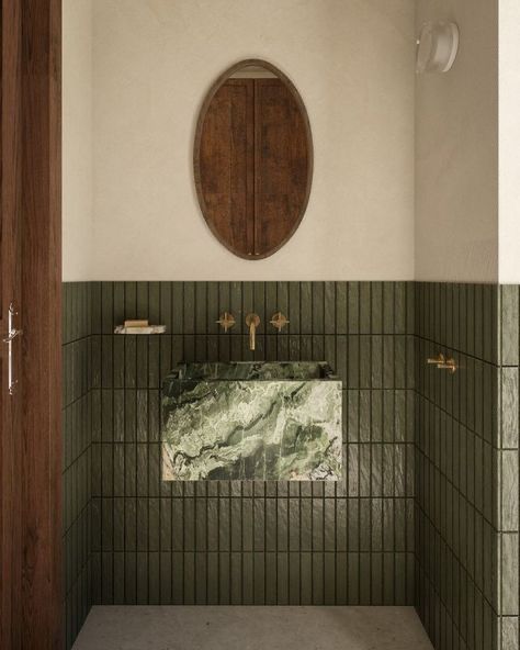 a green tiled bathroom with a round mirror above the sink and wooden door on the wall