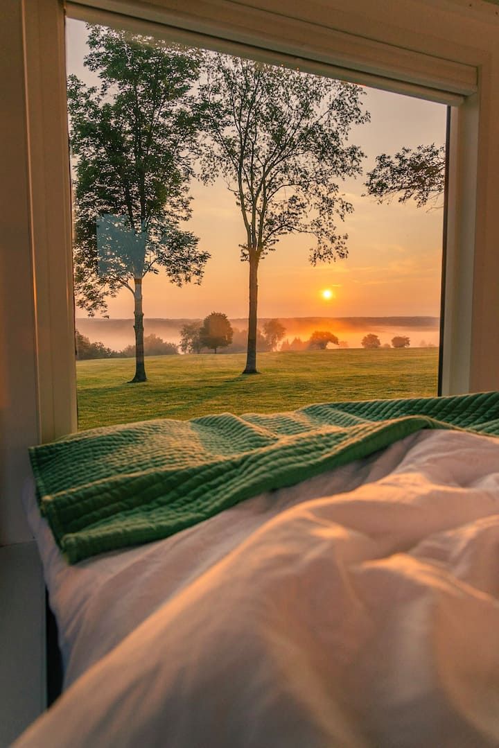 the sun is setting in front of a window that looks out onto a grassy field