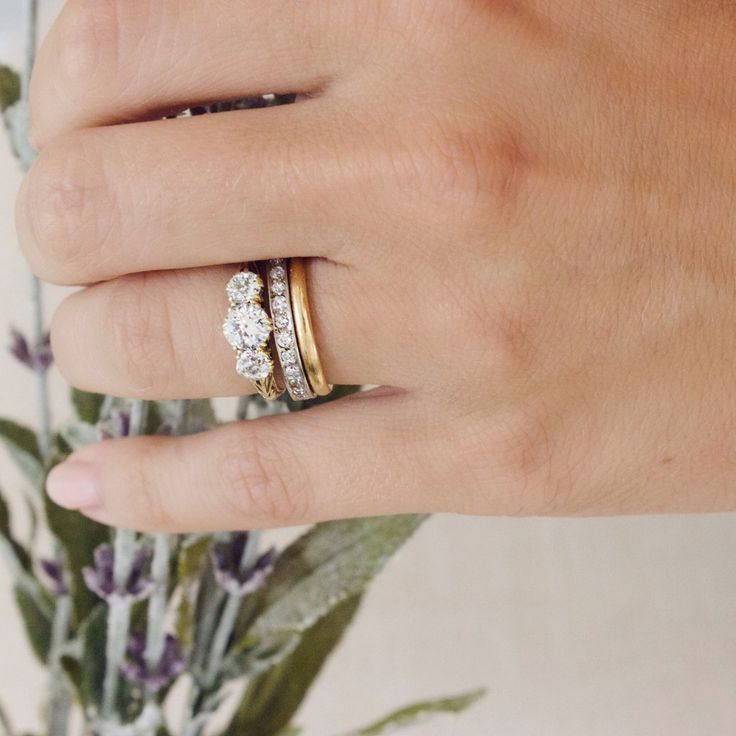 a woman's hand with two rings on her finger and flowers in the background