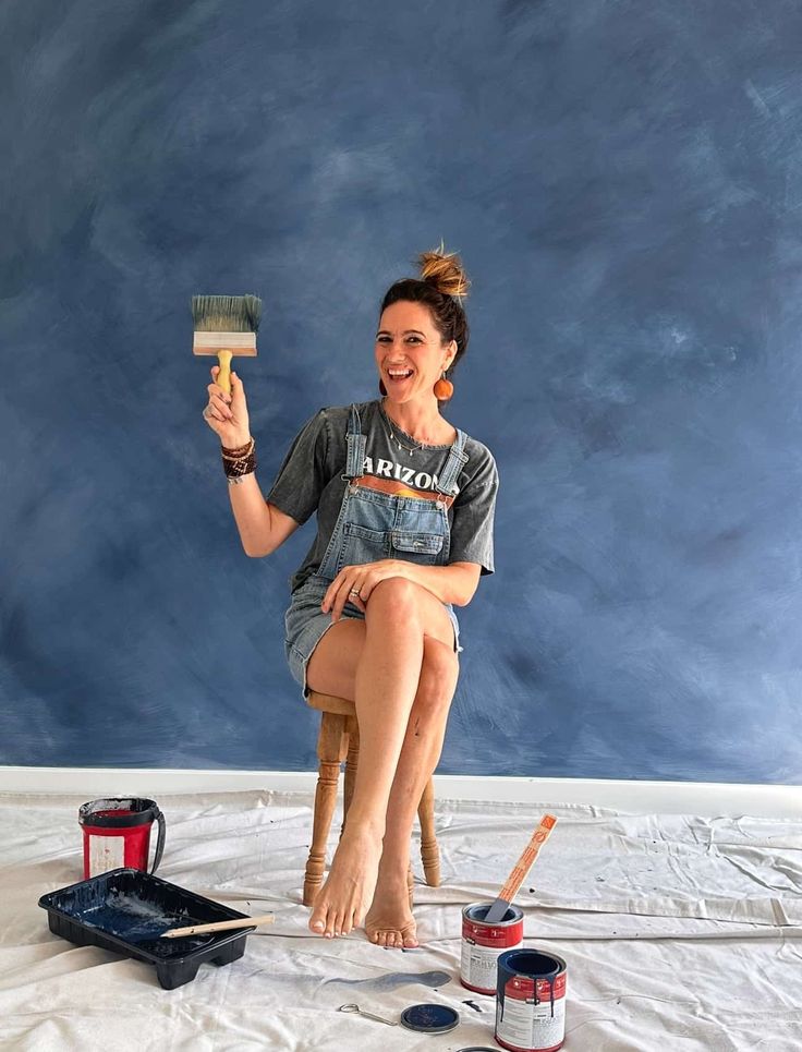 a woman sitting on top of a stool holding a paint brush