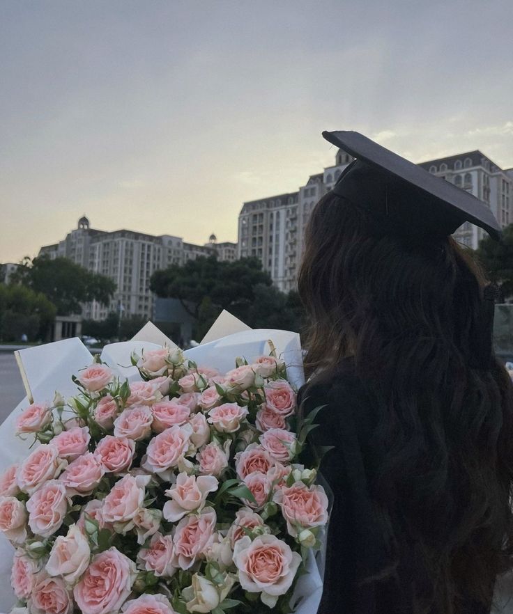 a woman wearing a graduation cap and gown holding a bouquet of flowers in front of her