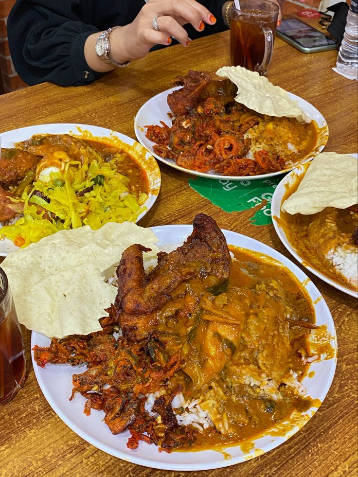 three plates of food sitting on top of a wooden table next to a glass of beer