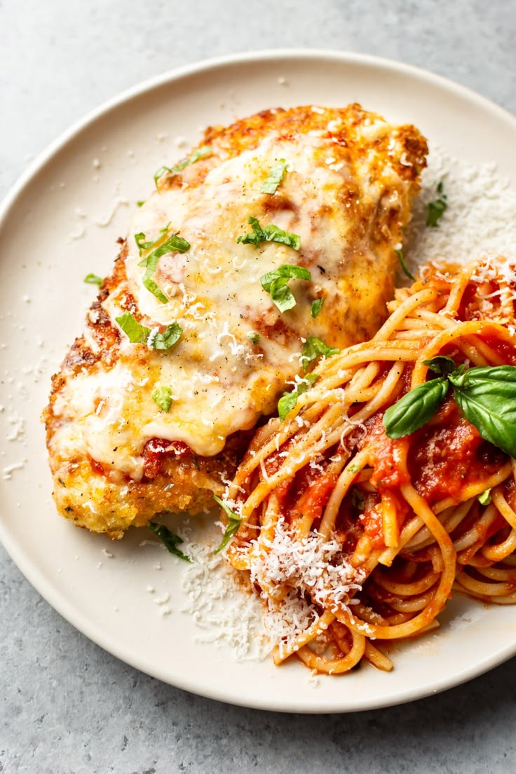 two pieces of chicken parmesan and pasta on a white plate with basil garnish