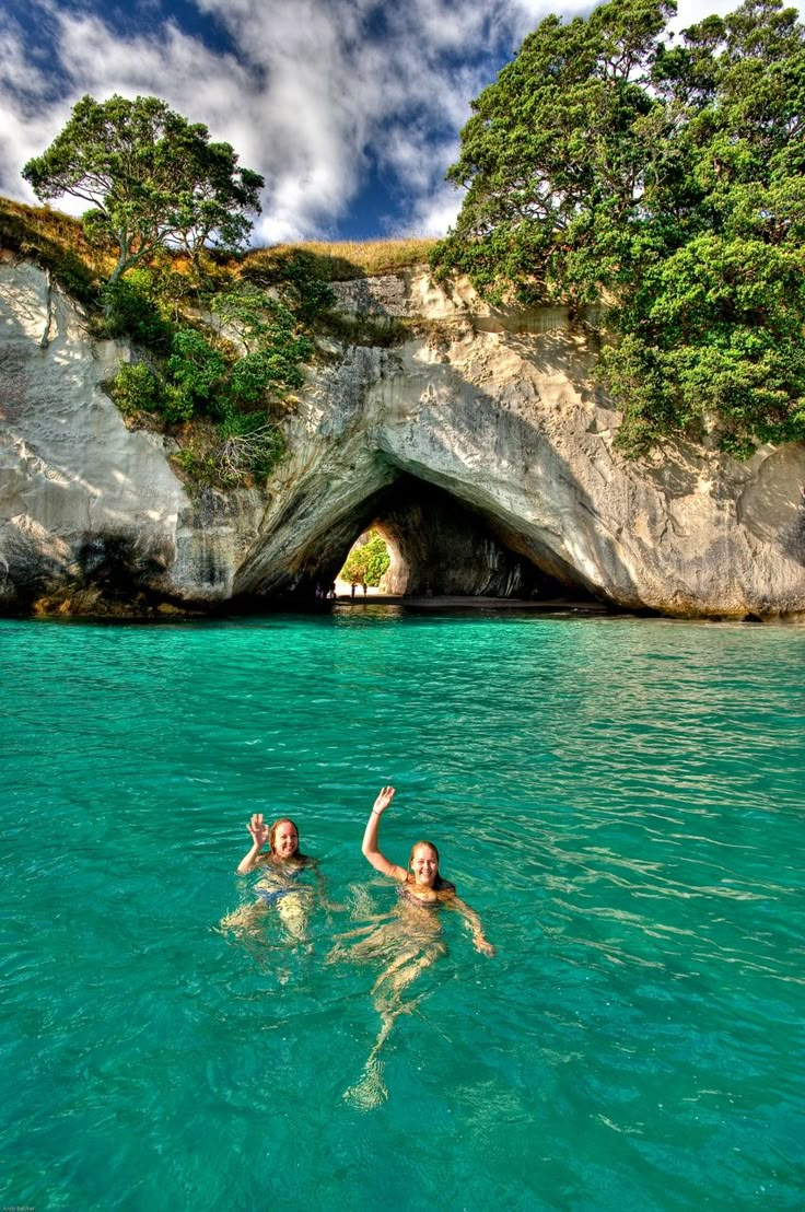 two people swimming in the ocean near a cave