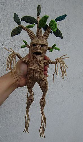 a person is holding up a knitted doll with leaves on it's head