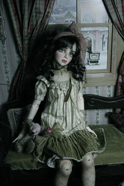 a doll sitting on top of a green bench in front of a window with curtains