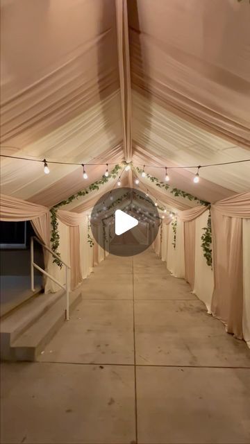 the inside of a tent with white drapes and string lights