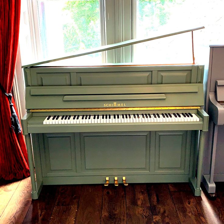 a green piano sitting in front of a window next to a red curtain and wooden floor