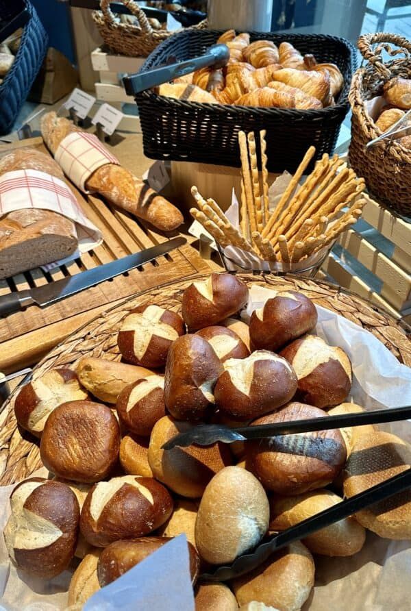 breads and pastries on display in baskets at a buffet table with utensils