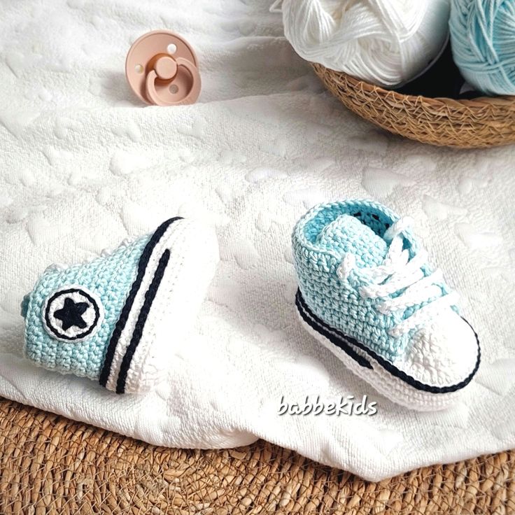 two crocheted shoes sitting on top of a white blanket next to balls of yarn