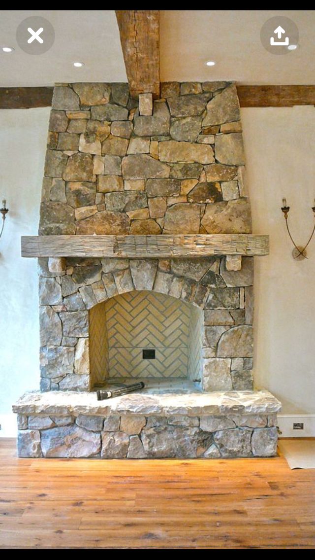 a large stone fireplace in the middle of a room with wood floors and exposed beams