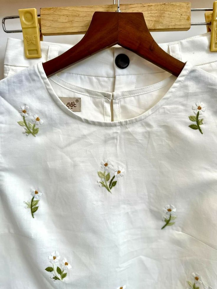 a white shirt with flowers on it hanging from a wooden hanger