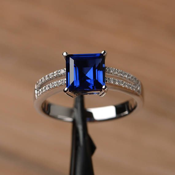 an engagement ring with a blue stone surrounded by white diamonds on a wooden table top