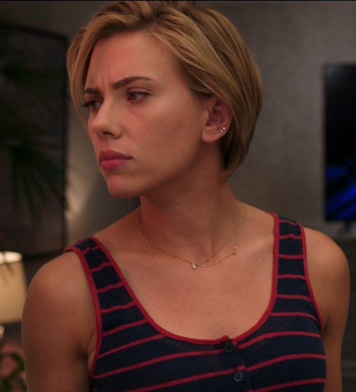 a woman with short hair wearing a tank top and looking off to the side while standing in a living room