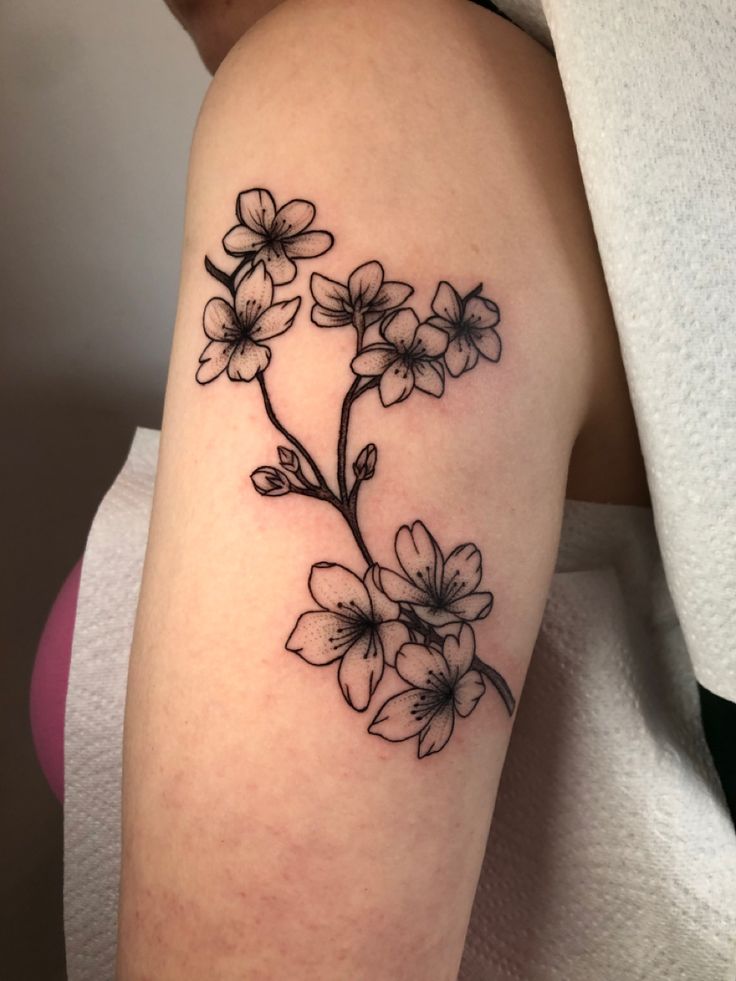 a black and white flower tattoo on the right arm, with small flowers growing out of it