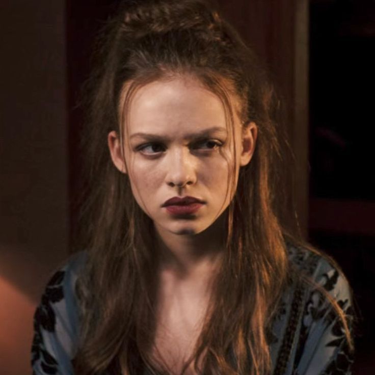 a woman with long hair and makeup looks at the camera while standing in a dark room