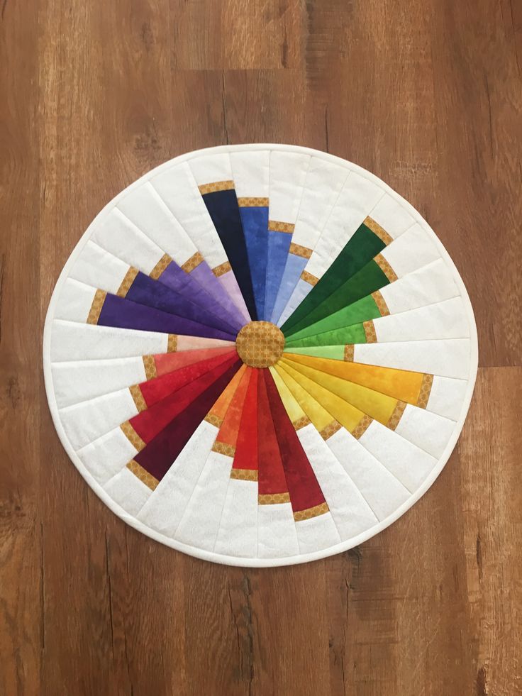 a white circular rug with multiple colors of fabric in the center on a wooden floor