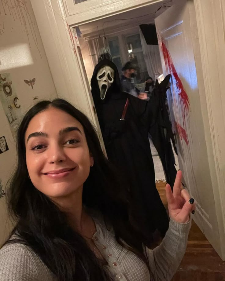 a woman standing in front of a door with a creepy mask on her face and another person wearing a costume behind her