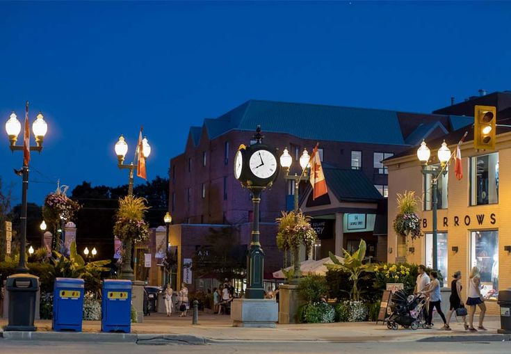 people are walking on the sidewalk in front of some buildings at night with a large clock