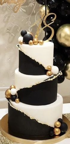 a three tiered black and white cake with gold decorations on the top is surrounded by balloons