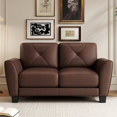 a brown leather love seat sitting in front of a wall with framed pictures on it