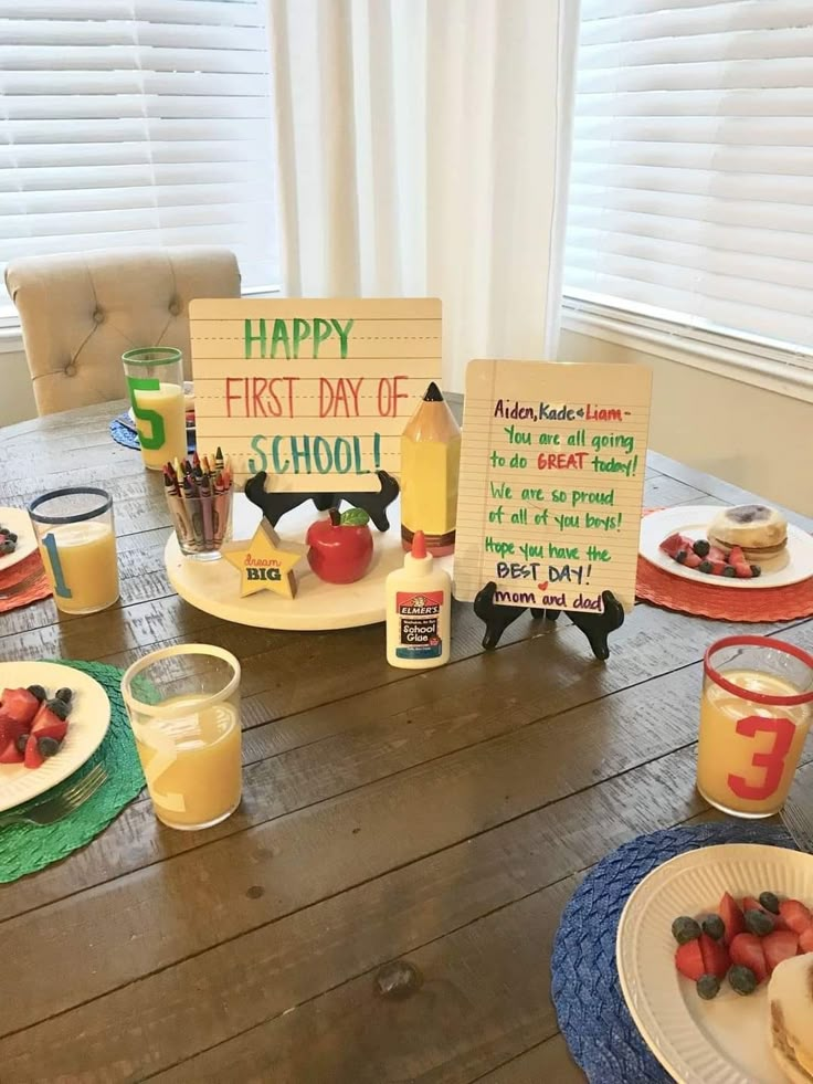 a wooden table topped with plates and cups filled with fruit next to a sign that says happy first day of school