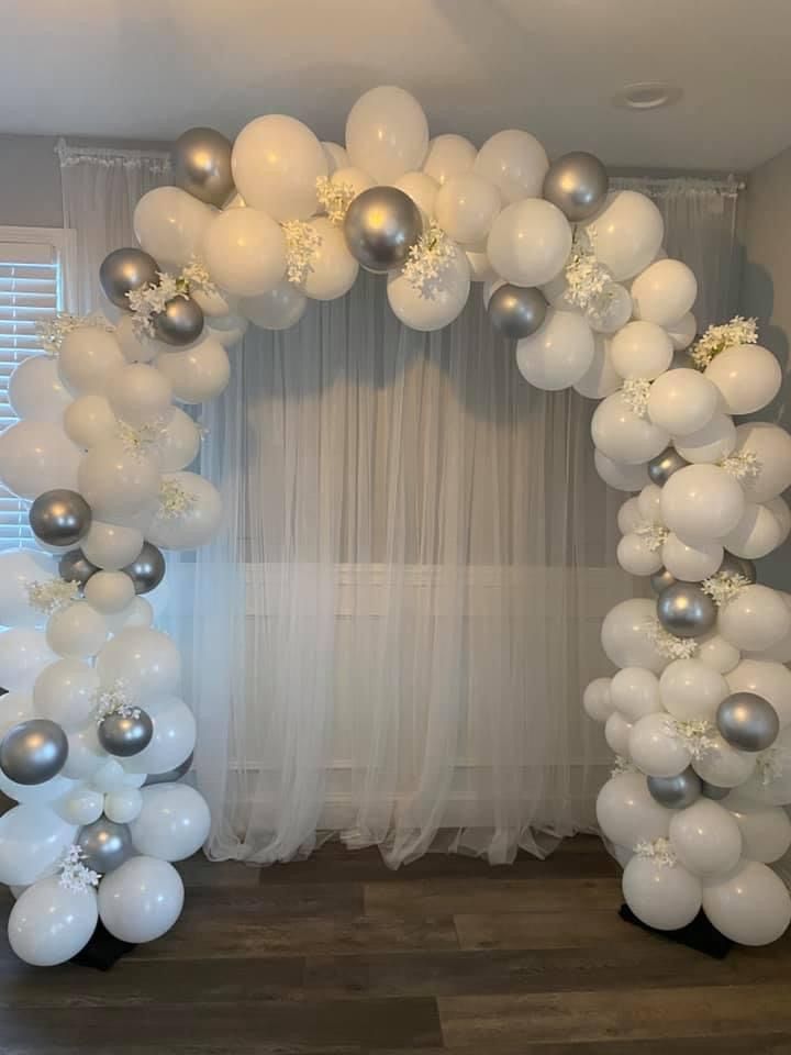 a white and silver balloon arch in front of a window