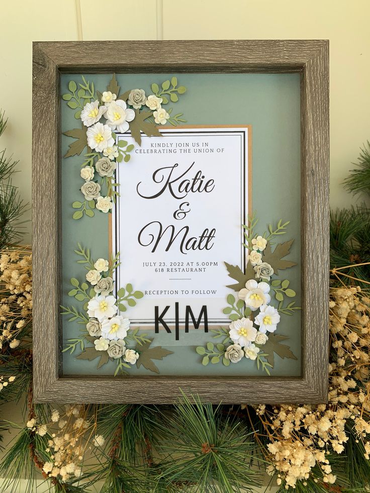 a wooden frame with paper flowers and greenery around it on top of a mantle