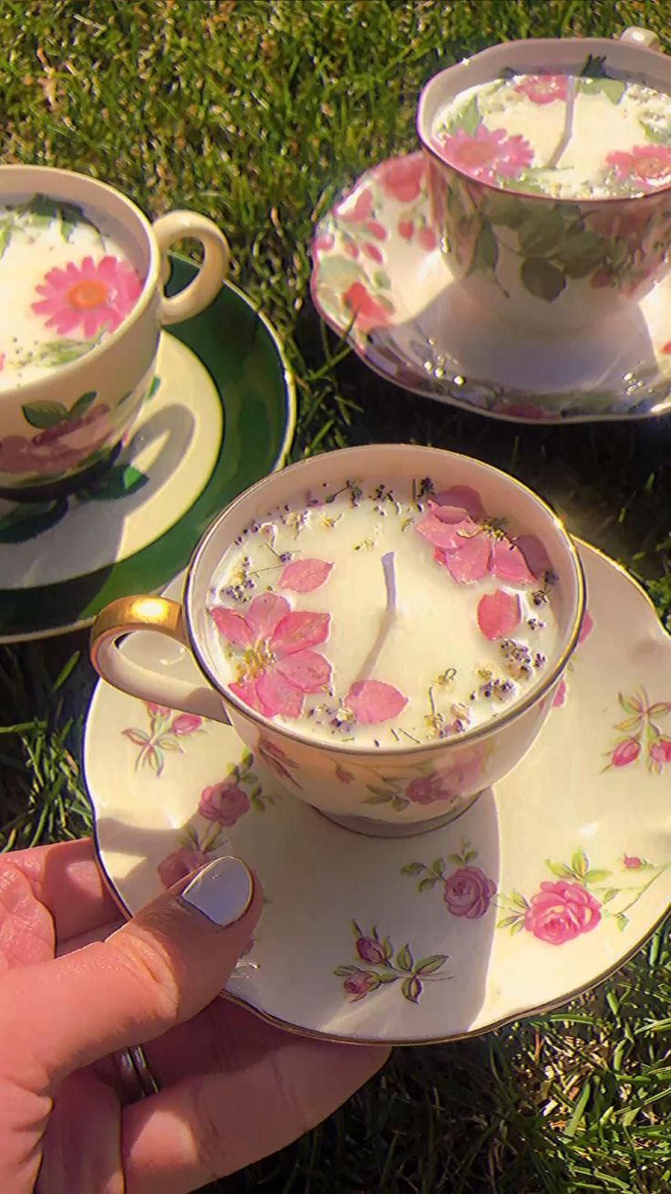 two tea cups and saucers with pink flowers on them are being held by someone's hand