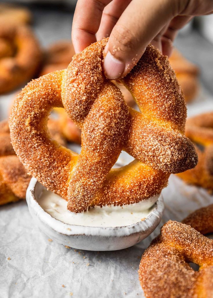 a person dipping some sugar on top of doughnuts in a small white bowl