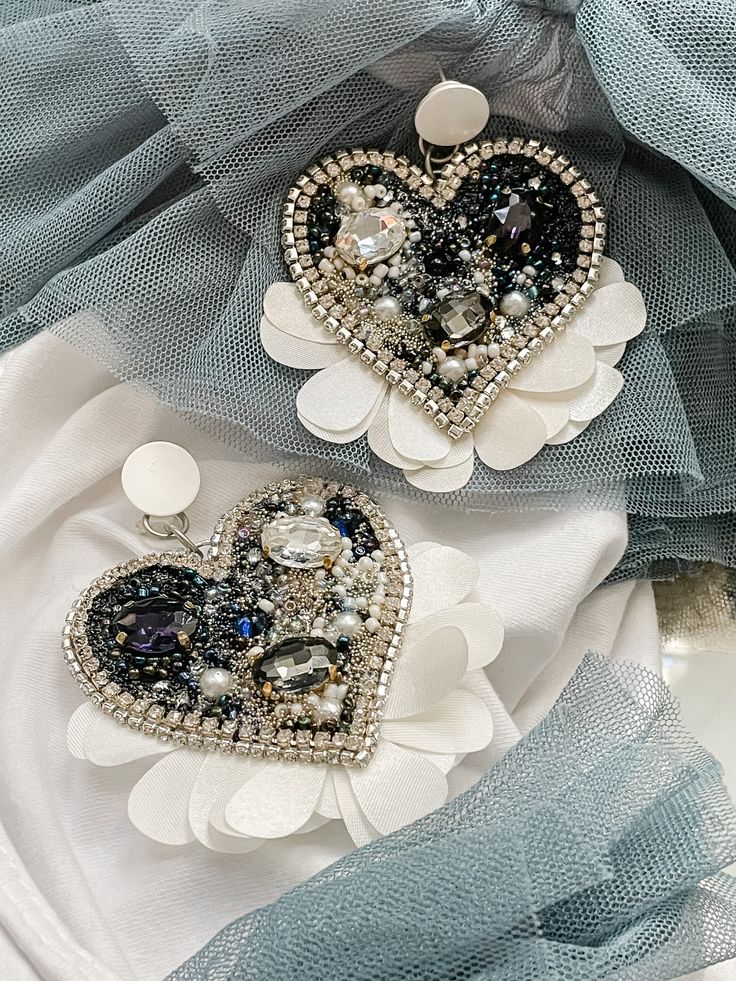 two heart shaped brooches are sitting on a white and blue cloth with pearls