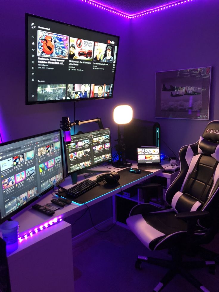 a room with two computer monitors and three television screens on the wall, all lit up by purple lighting